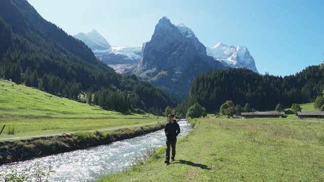 View of Rosenlaui with male tourist walking along Reichenbach river and wetterhorn glacier mountain in Bern, Switzerland