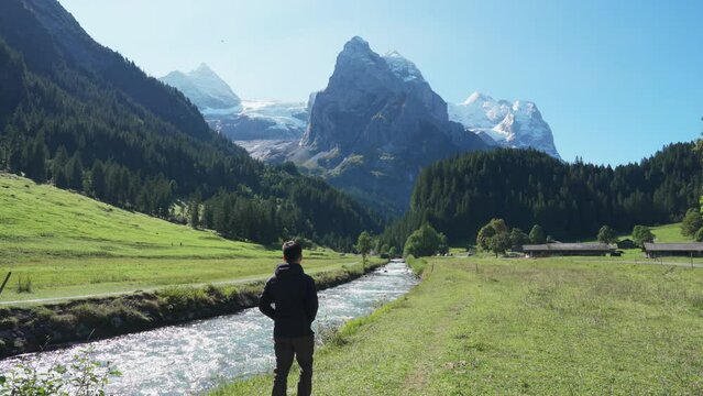 View of Rosenlaui with male tourist walking along Reichenbach river and wetterhorn glacier mountain in Bern, Switzerland