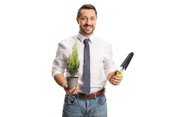 Smiling professional mam holding a small tree in a pot and a spade