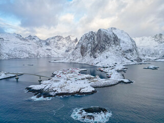 Aerial view of Lofoten island Norway. The winter season of sunrise fishing village of Reine with snowscape mountain peak reflect on water. Norway with red rorbu houses. With falling snow in winter.
