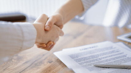 Business people shaking hands above contract papers just signed on the wooden table, close up. Lawyers at meeting. Teamwork, partnership, success concept - 675995027