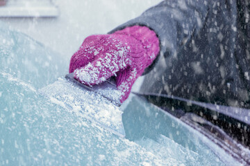 Winter Driving - Close-up of a woman's gloved hand using an ice scraper to remove ice from the...