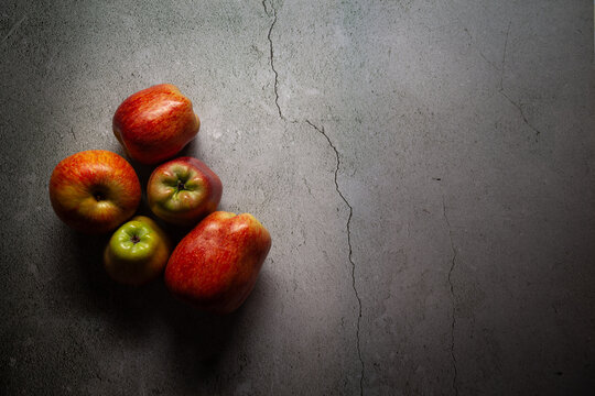 Whole apples of different sizes are placed over a marble table. Dark and moody scene.