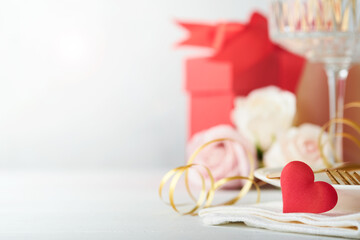 Valentines Day or Romantic dinner concept. Romantic table setting, silverware,  wine glasses, gift box, roses and symbol of love red heart on white background. Romantic Dinner Valentines Day concept.