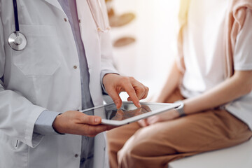 Doctor and patient in clinic. Friendly physician using tablet computer near a young woman. Medicine concept