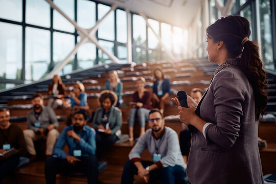 Female business leader talks to group of seminar attendees at convention center.