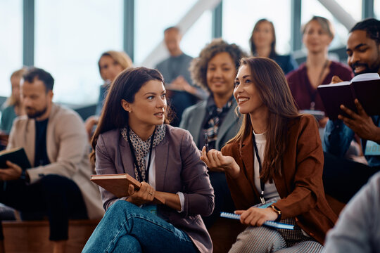 Happy female entrepreneurs talk while attending business seminar at convention center.