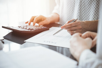 Woman accountant using a calculator and laptop computer while counting taxes for a client. Business...