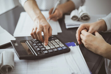 Woman accountant using a calculator and laptop computer while counting taxes for a client. Business audit and finance concepts