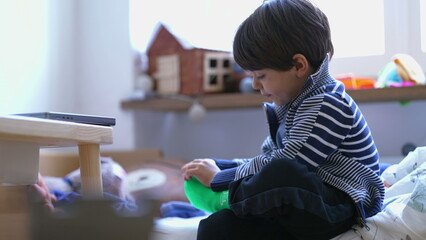 Child putting on sock seated by bedside. Small boy dressing himself. Kid getting ready to start the day routine