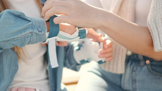 Mon helping her daughter in the park rollerblading enjoying there time together helping her daughter put on the safety on her hands
