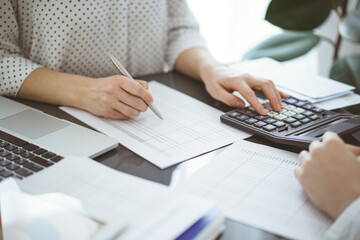 Woman accountant using a calculator and laptop computer while counting taxes with a client or a colleague. Business audit team, finance advisor