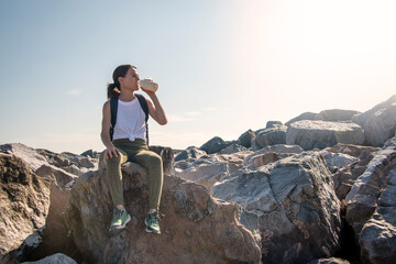 A woman hiker sits on the rock resting in the sun, drinking water from a bottle
