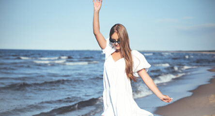 Fototapeta na wymiar Happy blonde woman having fun on the ocean beach in a white dress and sunglasses
