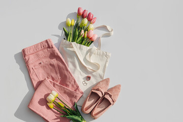 Fashion spring outfit. Pale pink jeans with bouquet of tulips flowers in bag,  and loafers. Women's...