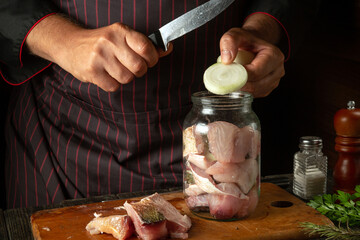 The cook prepares herring in the kitchen from fish steaks and aromatic spices. Canning fish in a...