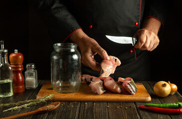 The chef cuts raw fish into steaks before preparing herring in a jar. Working environment on the...