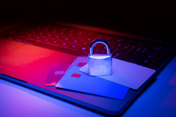 Closeup of a padlock on a laptop and credit card illuminated with blue and red light. Phishing, cybersecurity danger or ransomware attack. Encrypted privacy in e-comerce