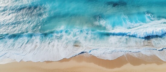 Fototapeta na wymiar In the aerial photograph the breathtaking beach landscape with its azure waves crashing against the sandy shore creates a captivating background against the textured backdrop of nature entic