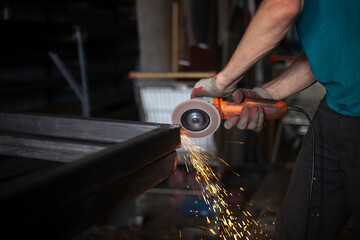 Metal processing. Grinder in hand. Worker holds tool. Creation of steel structure.