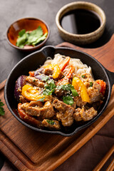 Asian pork with vegetables and glass noodles in a pan on the black background vertical photo