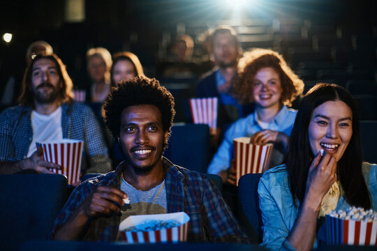 Young people sitting at the cinema watching a movie and eating popcorn