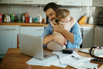 Little young daughter hugging father in kitchen with documents on desk - obrazy, fototapety, plakaty