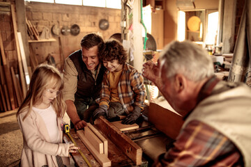 Little children learning carpentry from adults in workshop