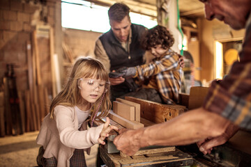 Little children learning carpentry from adults in workshop