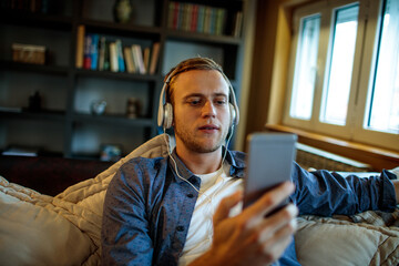 Young man with headphones holding smartphone in living room