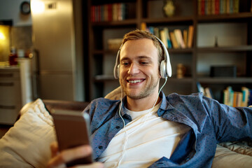 Young man with headphones holding smartphone in living room