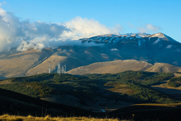 Naklejka premium Wind farm with turbines on the mountains. Eco-sustainable industry with nature-friendly technologies for clean energy in a better environment. Conceptual mountainous landscape