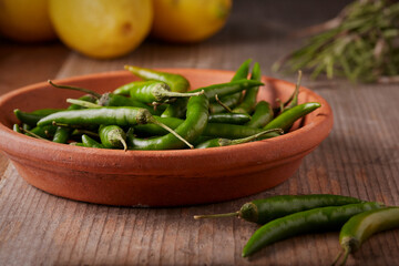 Freshly picked green finger peppers in a dish with some lemons and herbs in the background.