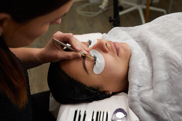 Close up of false eyelash extension application with tweezers