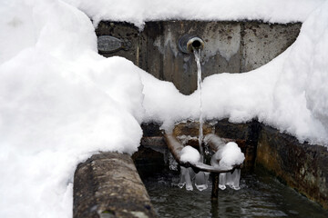 Regulated natural spring or source of water arranged into a fountain in winter captured in front view. It is almost covered with snow and there is a lot of copy space. 