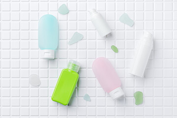 Travel size cosmetic bottles for cream, lotion, shampoo, tonic, serum, oil. White tile background.