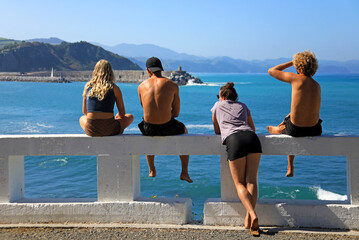 jovenes pareja sentados mirando al mar desde un pretil zumaia verano getaria país vasco  - 676046838