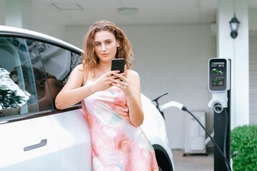 Modern eco-friendly woman recharging electric vehicle from home EV charging station. Innovative EV...
