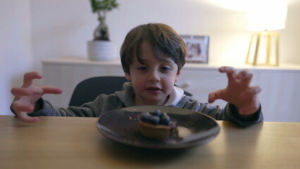 Small boy grabbing blueberry cake snack from plate. Child eating sugar yet healthy food dessert...