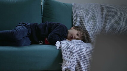 Small boy laid on sofa couch watching cartoons on screen off-camera. Child hypnotized by...