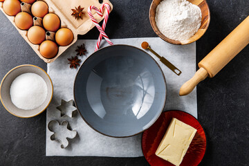 baking, cooking and christmas concept - close up of ceramic bowl, molds, rolling pin and ingredients on black table top - obrazy, fototapety, plakaty