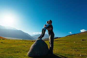 Happy father hugs his son standing on big stone in the mountains - 676061869
