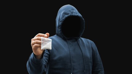 Faceless man in a hood holds transparent plastic bag with white powder hard drugs on dark background, anonymous drug dealer or gangster sells narcotics - obrazy, fototapety, plakaty