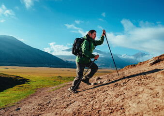 Man hiker with trekking poles and backpack climbing up the mountain