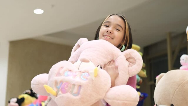 A little girl in a lilac elegant dress against the background of soft toys in a store. A child chooses a toy as a gift