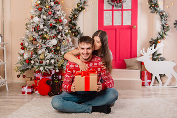 Obraz na płótnie Canvas A beautiful couple on a Christmas background gives each other gifts. Young man and woman are preparing for the holiday.