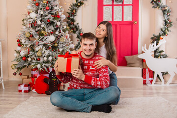 Obraz na płótnie Canvas A beautiful couple on a Christmas background gives each other gifts. Young man and woman are preparing for the holiday.