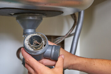 clogged sink pipe in hand,a plumber cleans a clogged siphon pipe of a sink in the kitchen - obrazy, fototapety, plakaty