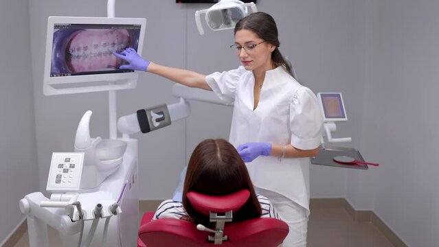 Caucasian dentist woman explaining x-ray on screen to female patient at clinic