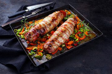 Gebratenes Mangalica Schweinefilet gefüllt mit gehackten Wallnüssen und Kürbis und umwickelt mit Speckmantel serviert mit Gemüse als close-up auf einem Backblech 